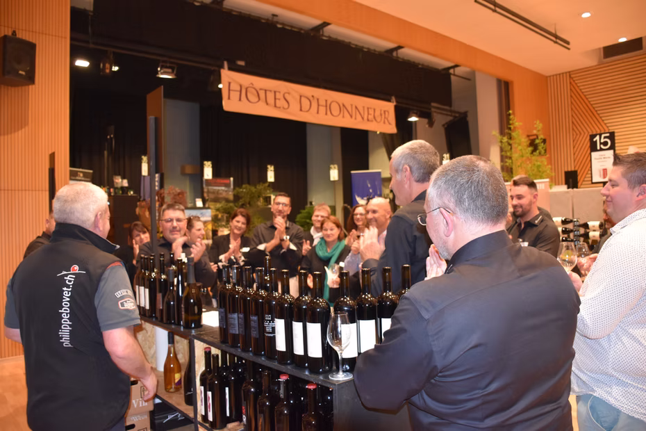 Présentation des hôtes d'honneur devant une rangée de bouteilles de vin.